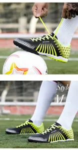 Detailed side view of black and yellow TF turf soccer shoes shown on a green soccer field
