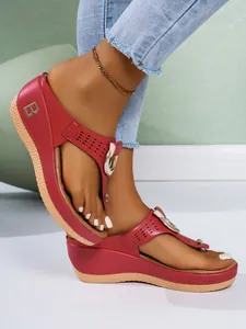 Detalle de sandalias rojas con cuña, con un elegante logo 'B' metálico y hebilla.
