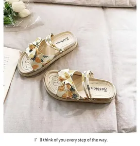 Detail view of cream platform sandals with vibrant pineapple print and bow detail
