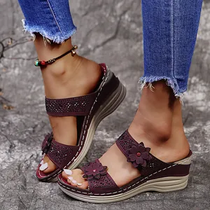 Close-up of maroon wedge sandals with flower and rhinestone details on a model.