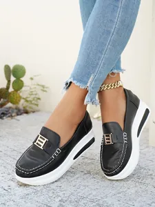 Close-up of black PU leather loafers with metal buckle and thick white sole on model.