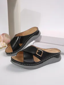 Detail showing black cross-strap sandals with gold buckle and grey thick wedge sole.