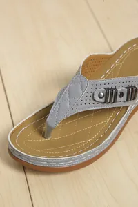 Dettaglio di sandali infradito grigi con soletta marrone trapuntata e decorazioni