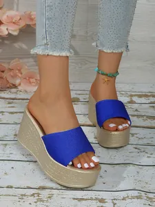 Gros plan montrant la bride en satin bleu et la texture tissée or des sandales compensées.