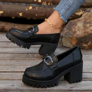 Zwarte loafers met plateauzool en blokhak met metalen gesp op houten dek.