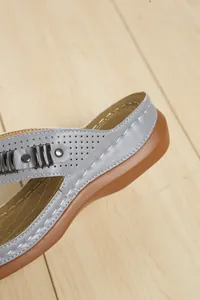 Vista dettagliata del sandalo grigio argento con decorazioni in metallo e suola marrone.
