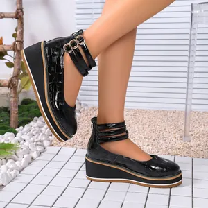 Gros plan sur des chaussures compensées en cuir verni noir à motif crocodile et brides.