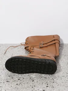 Detailed shot of brown PU tall boots featuring metallic buckles and a textured black sole