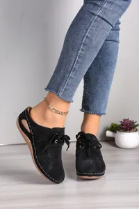 Macro view of black lace-up mule shoes featuring laser-cut details and sturdy wedge soles.