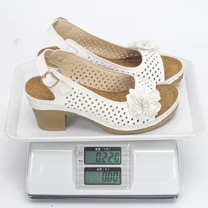 Lightweight white floral high heel sandals with ankle strap on a digital scale showing weight