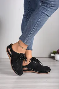 Close-up of black suede hollow-out mules with lace-up detail and wedge sole