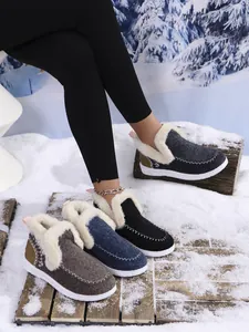 Detail view of various colorful fur-lined warm winter boots on a snow and wood background