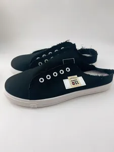 Vista lateral de zapatillas mule de lona negra con etiqueta decorativa y suela blanca