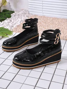 Vue détaillée de chaussures compensées en cuir verni noir à motif croco et brides