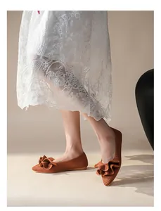 Nahaufnahme brauner gewebter Ballerinas mit Rüschenbesatz, getragen zu einem Spitzenkleid.
