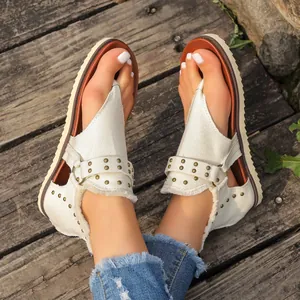 Close-up view of cream canvas thong sandals with metallic rivets on rustic wood.