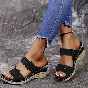Close-up of black wedge sandals with decorative flowers and sparkling rhinestones on model.