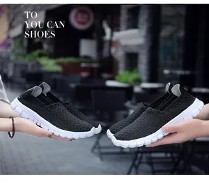Pair of breathable black woven elastic slip-on loafers held in hands outdoors.