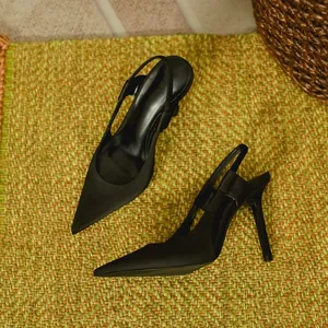 Elegant black satin pointed-toe slingback stiletto heels detail view on a textured mat