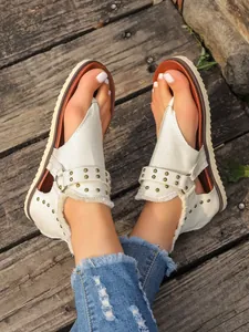 Detailed view of women's white canvas thong sandals with brass studs and back zipper