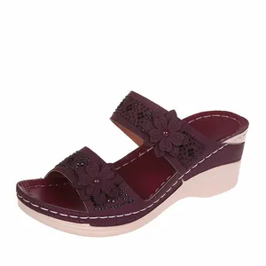 Detailed view of burgundy wedge sandals with 3D floral accents and white stitching