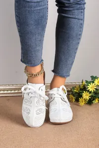 On-foot view of white hollow-out wedge loafers with lace-up details and gold anklet