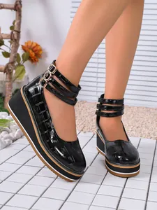 Gros plan sur des escarpins compensés en cuir verni noir avec triple bride à la cheville.