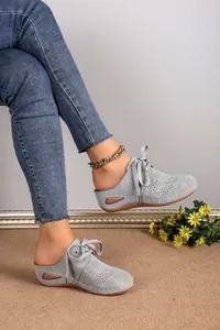 Close-up detail of grey hollow-out lace-up wedge mules worn by a model in a studio