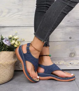 Blaue bestickte Zehentrenner-Sandalen an einem Modell mit floralem Hintergrund