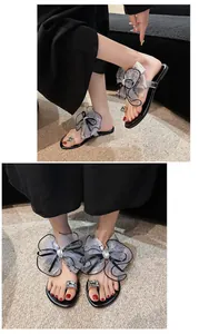 Detailansicht eleganter schwarzer flacher Sandalen mit Tüllschleifen und Kristallen.