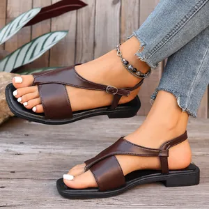 Detailed visual of brown cross-strap flat sandals with toe-clip design on wooden floor.