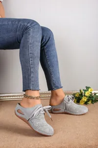 Detailed side view of grey laser-cut lace-up wedge mules with hollow floral patterns