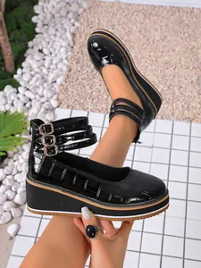 Détail de chaussures compensées en cuir verni noir avec triples brides à boucle.