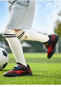 Action detail of children's breathable mesh soccer shoes with red flame pattern on turf.