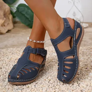 Detail of navy blue vintage Roman sandals with white stitching and cut-outs on pebbles.