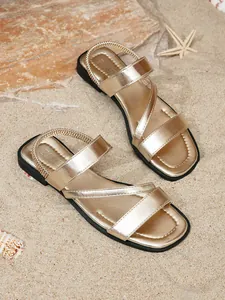 Detailed view of shiny gold flat Roman sandals on a sandy beach setting