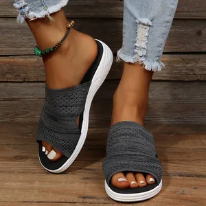 Detailed close-up of stylish women's dark grey knit flat slides on a rustic wood floor