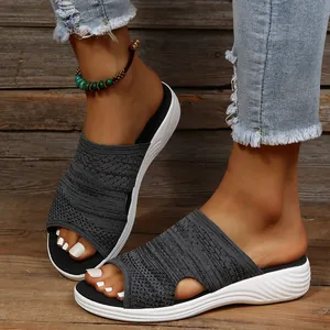 Close-up of women's grey knitted flat slippers with white wedge soles on wooden floor.
