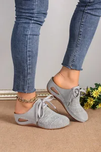 Detailed macro view of grey women's lace-up wedge mules with elegant laser-cut floral patterns.
