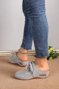Close-up detail showing grey lace-up wedge mules with hollow laser-cut floral patterns.