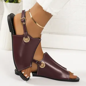Detailed view of women's dark burgundy flat open-toe sandals with gold buckle detail.