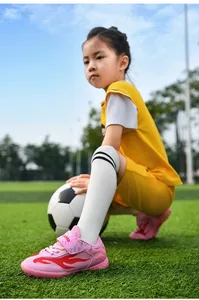 Close-up of pink breathable mesh kids soccer shoes worn on a green soccer field.