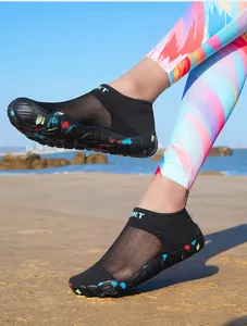 Close-up of lightweight black mesh water shoes with colorful splatter soles on a beach