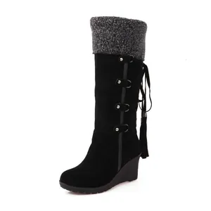 Vista lateral de botas de nieve negras con cuña, ribete de piel gris y con borlas