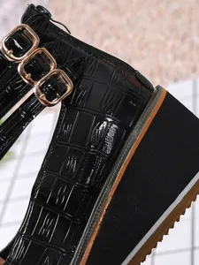 Gros plan de chaussures compensées en cuir verni noir avec motif croco et boucles