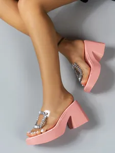 Close-up of pink platform slippers with clear strap and sparkly rhinestone buckle detail.