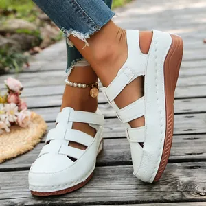 Detailansicht weißer Damen-Keilsandalen mit Ausschnitten auf einem Holzstegweg