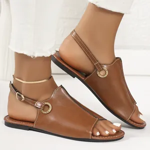 Detailed side view of brown flat leather sandals with circular metal ornament on a model