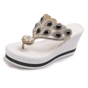 Chanclas de cuña blancas con piedras negras, perlas y detalles de pedrería brillantes.