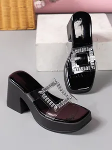 Detailed view of elegant black platform slippers with clear PVC strap and crystal buckle